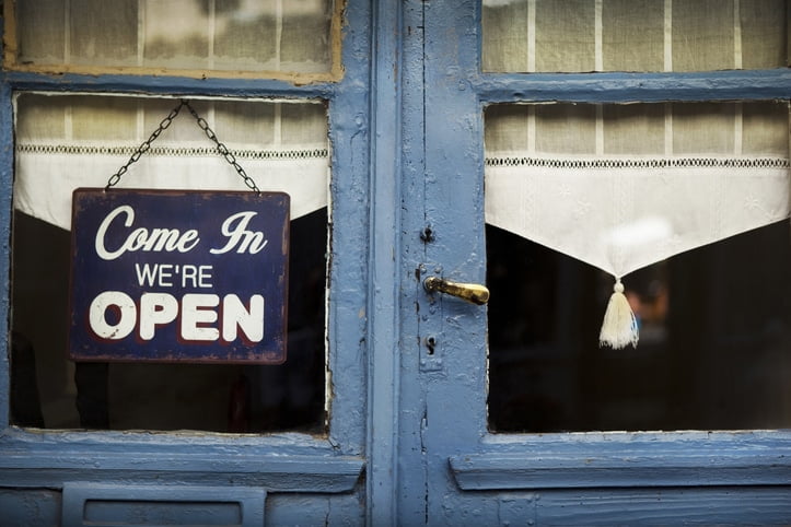 A blue door with a black sign with white lettering that says “Come in, we’re open” on the window.