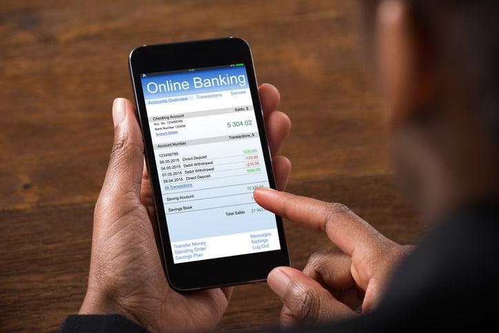 A pair of hands holding a smartphone with the words “online banking” at the top of the screen above a banking ledger.