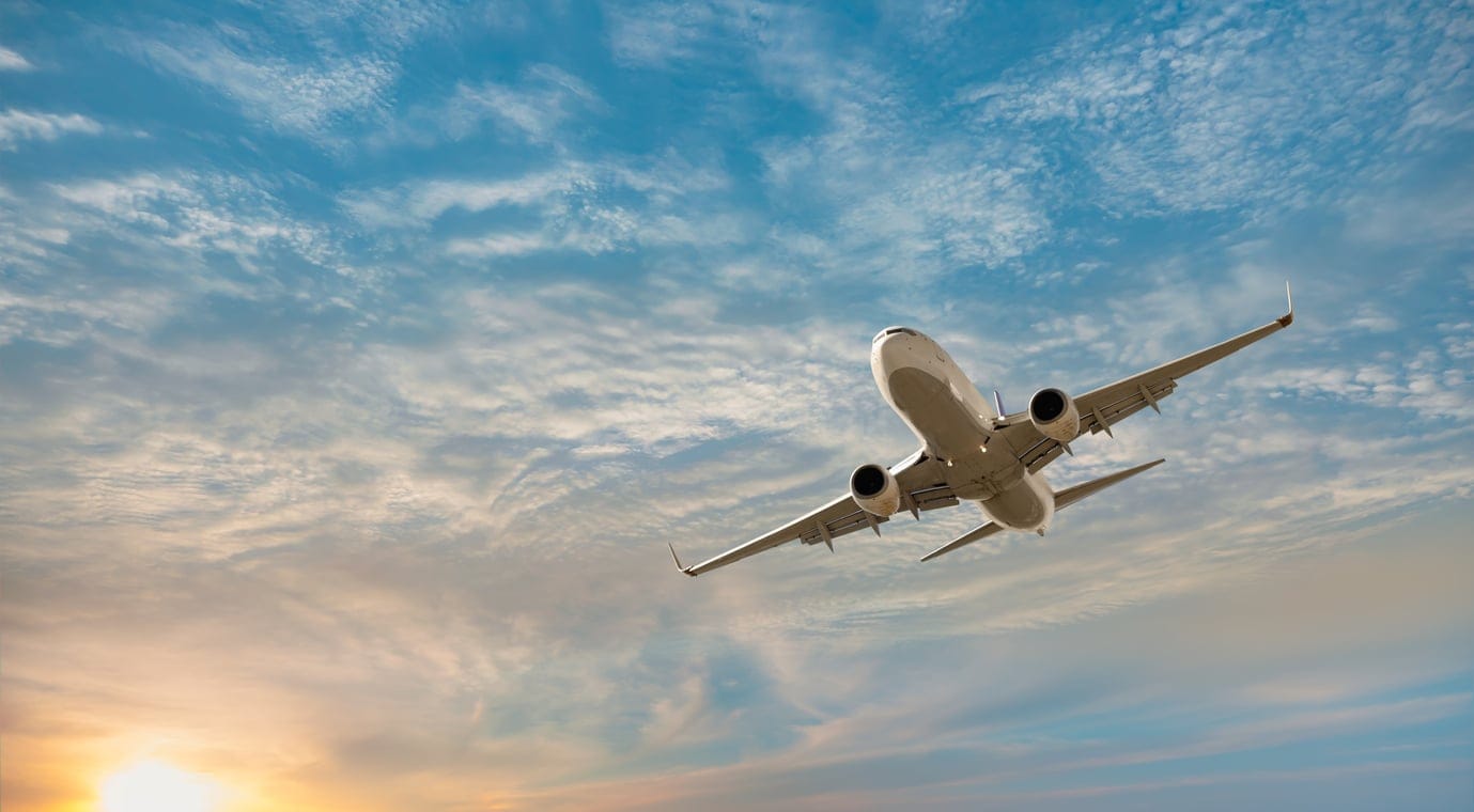 A large, white airplane in a cloudy winter sky being used for inexpensive travel this holiday season.