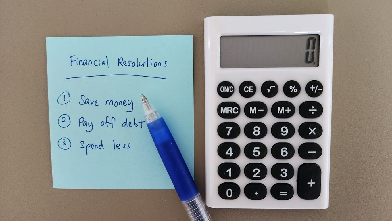 A calculator and a pen next to a blue sticky note with “Financial Resolutions” written at the top.
