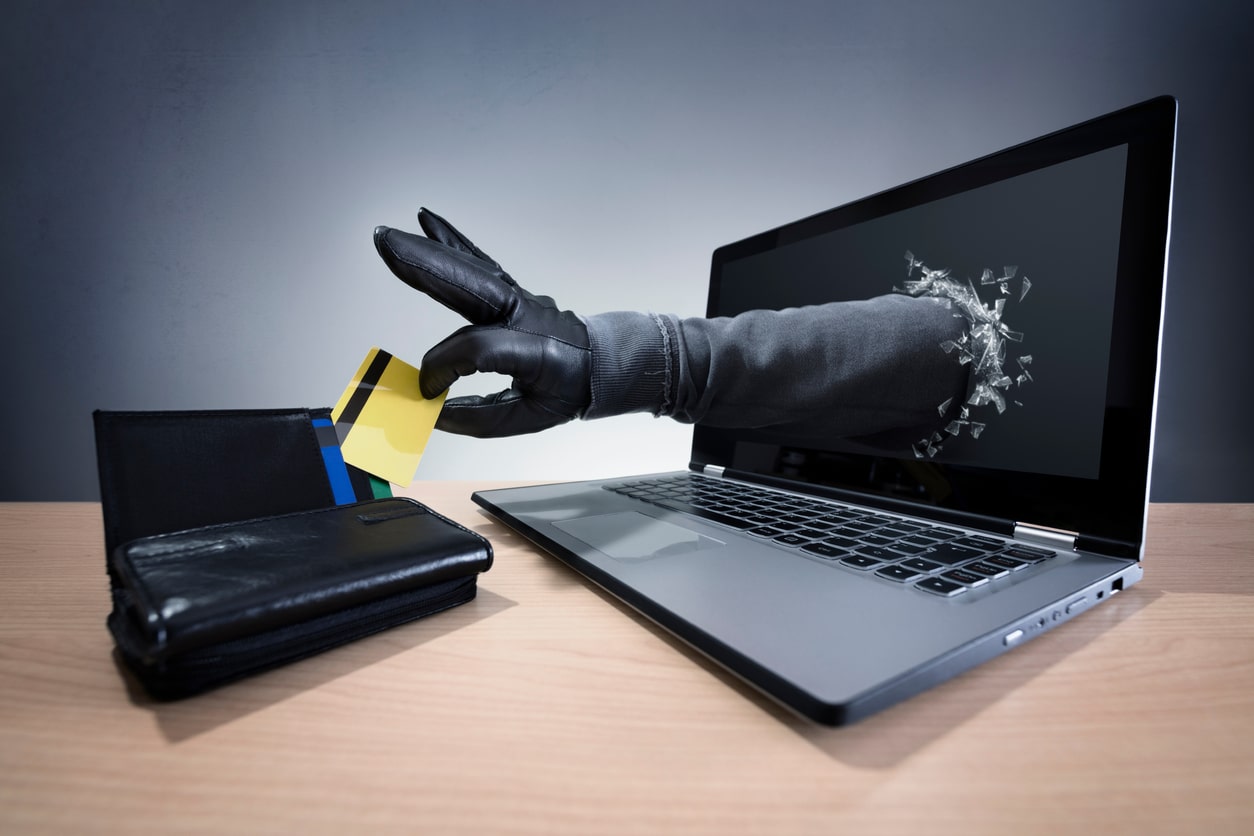 Hand bursting through computer screen to steal a credit card, visually representing the idea of digital identity theft.